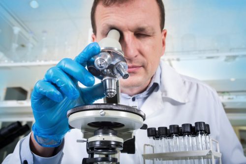 Scientist smiles as he finds secret cures with his microscope, such noble work.